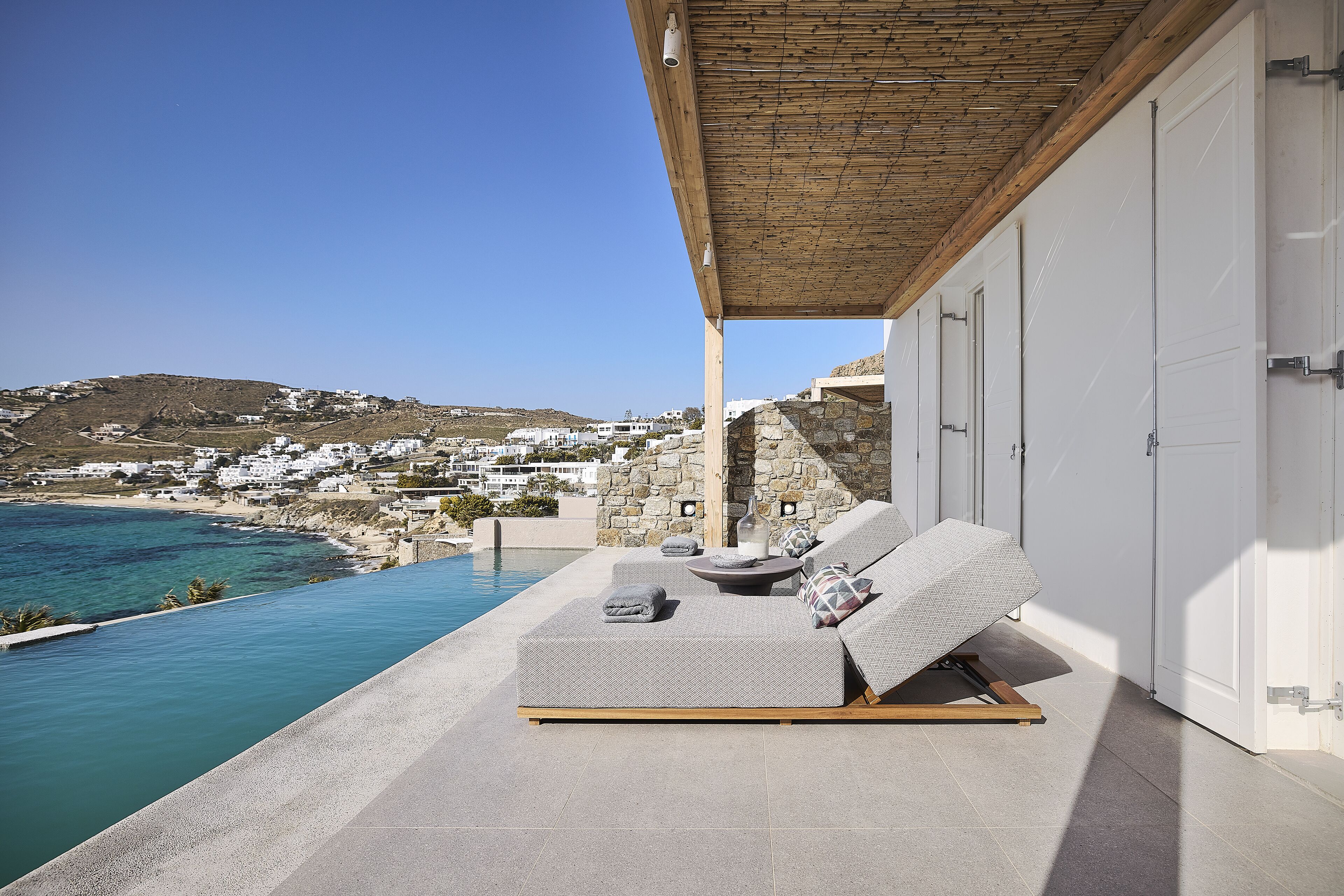 A modern outdoor seating area with a view of a coastal town and a pool.