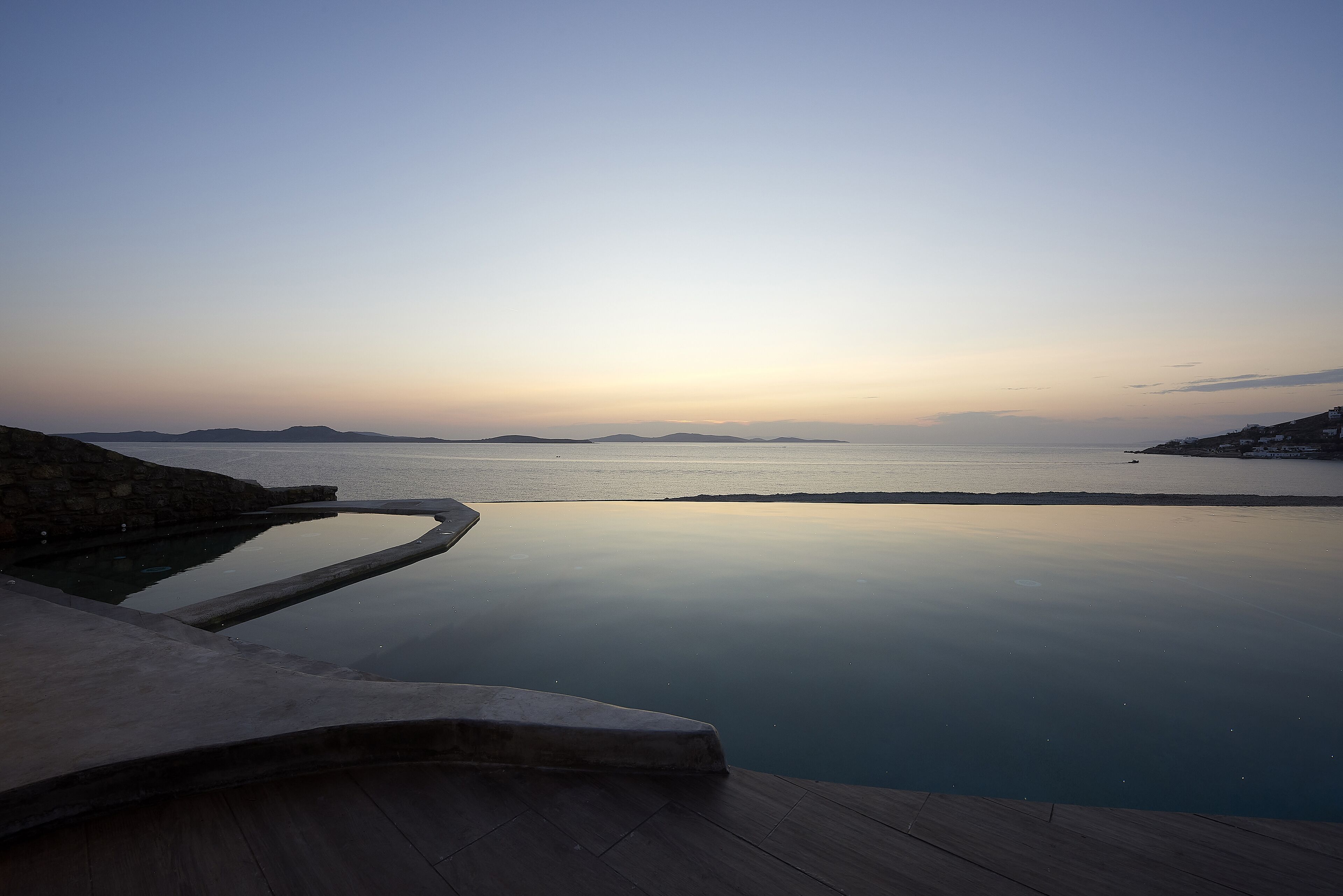 En lugn och avkopplande infinitypool med en klar utsikt över havet och avlägsna öar under solnedgången.