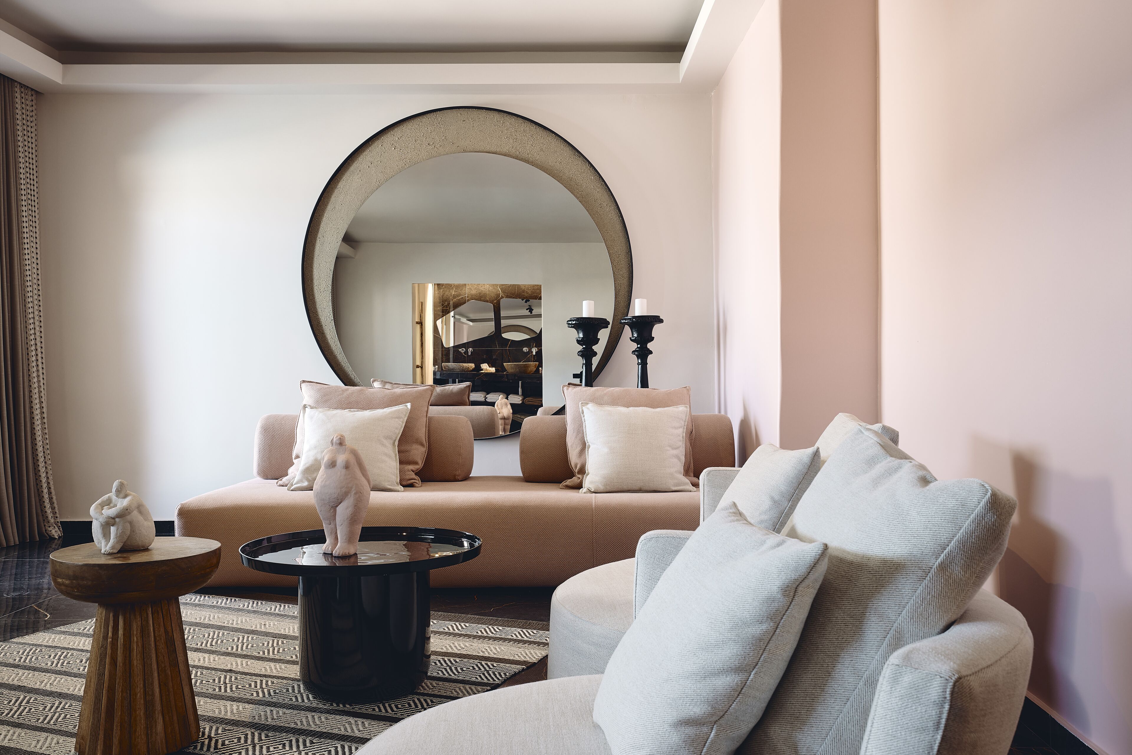 A modern living room with a beige sofa, a round coffee table, and a large mirror.