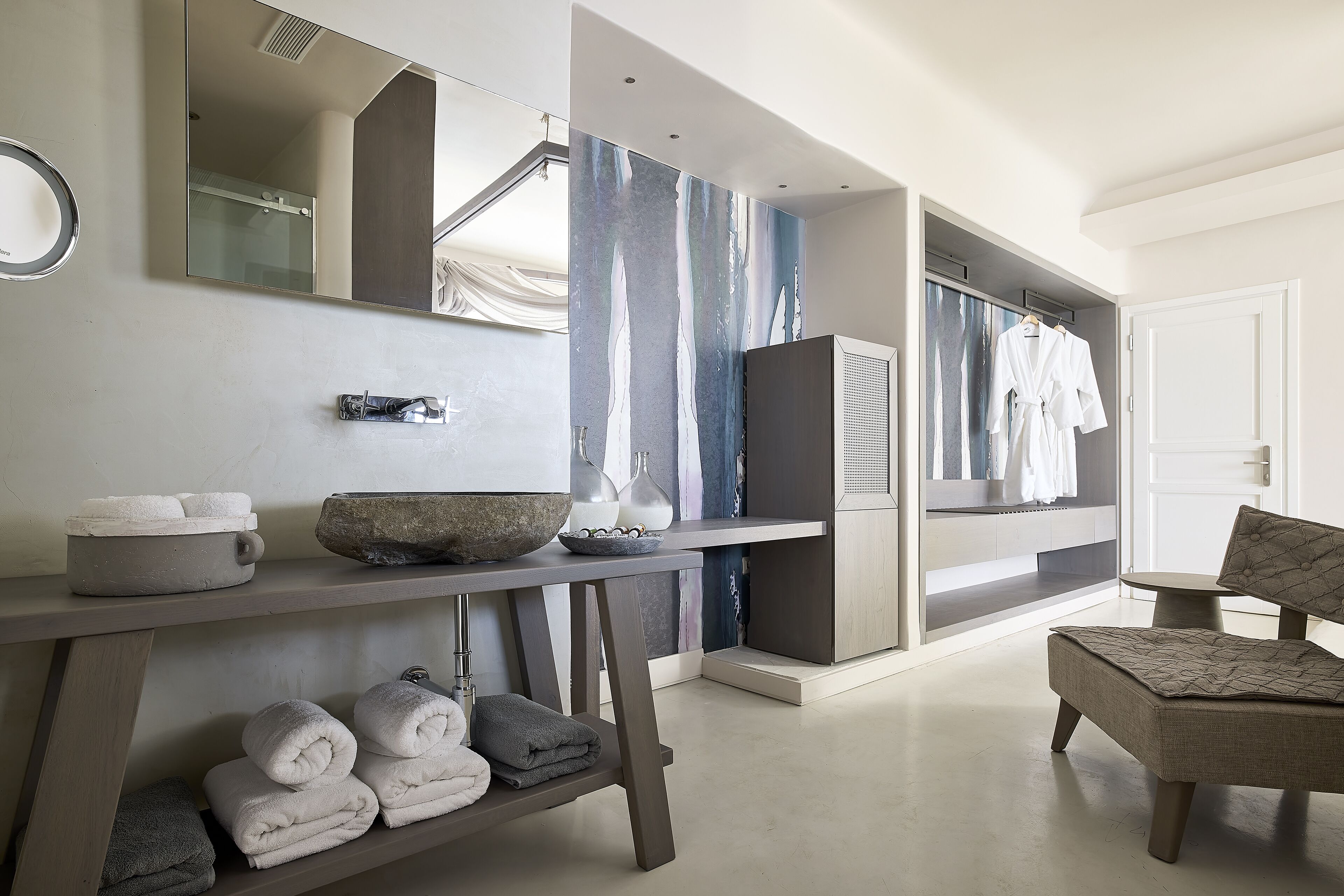 Une salle de bain moderne avec un grand miroir, un lavabo, des serviettes et une chaise.
