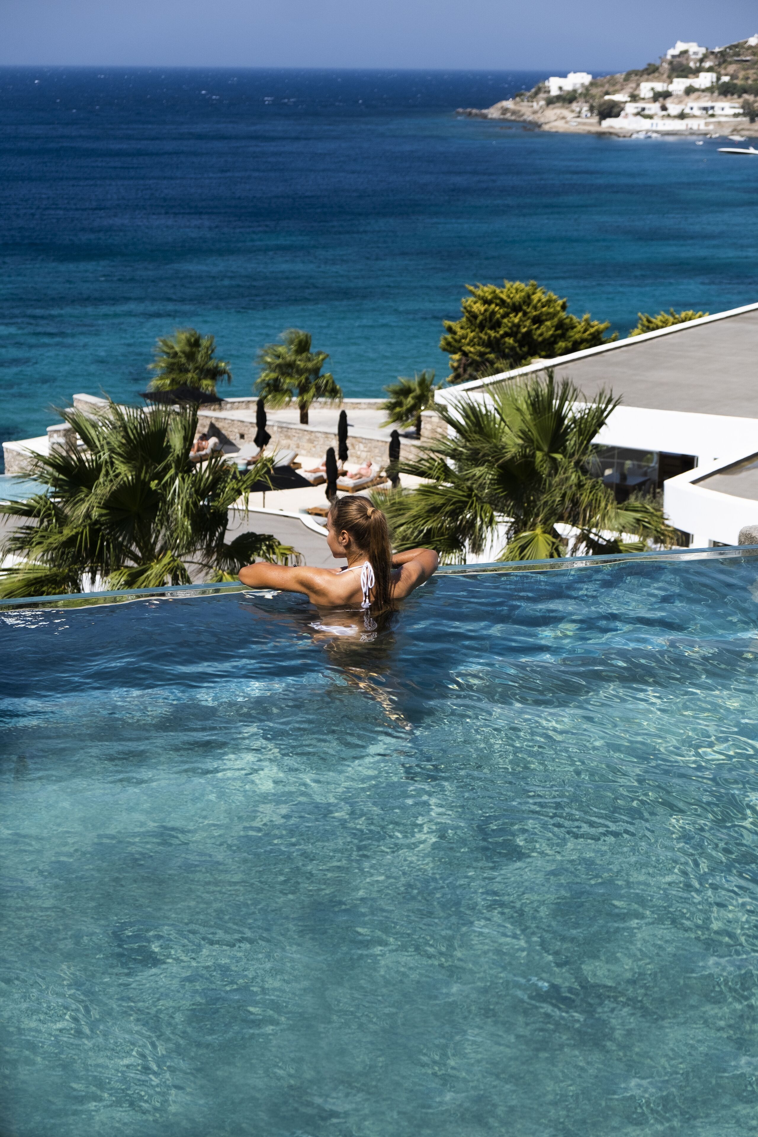 A pool with clear blue water, surrounded by palm trees and a view of the ocean.