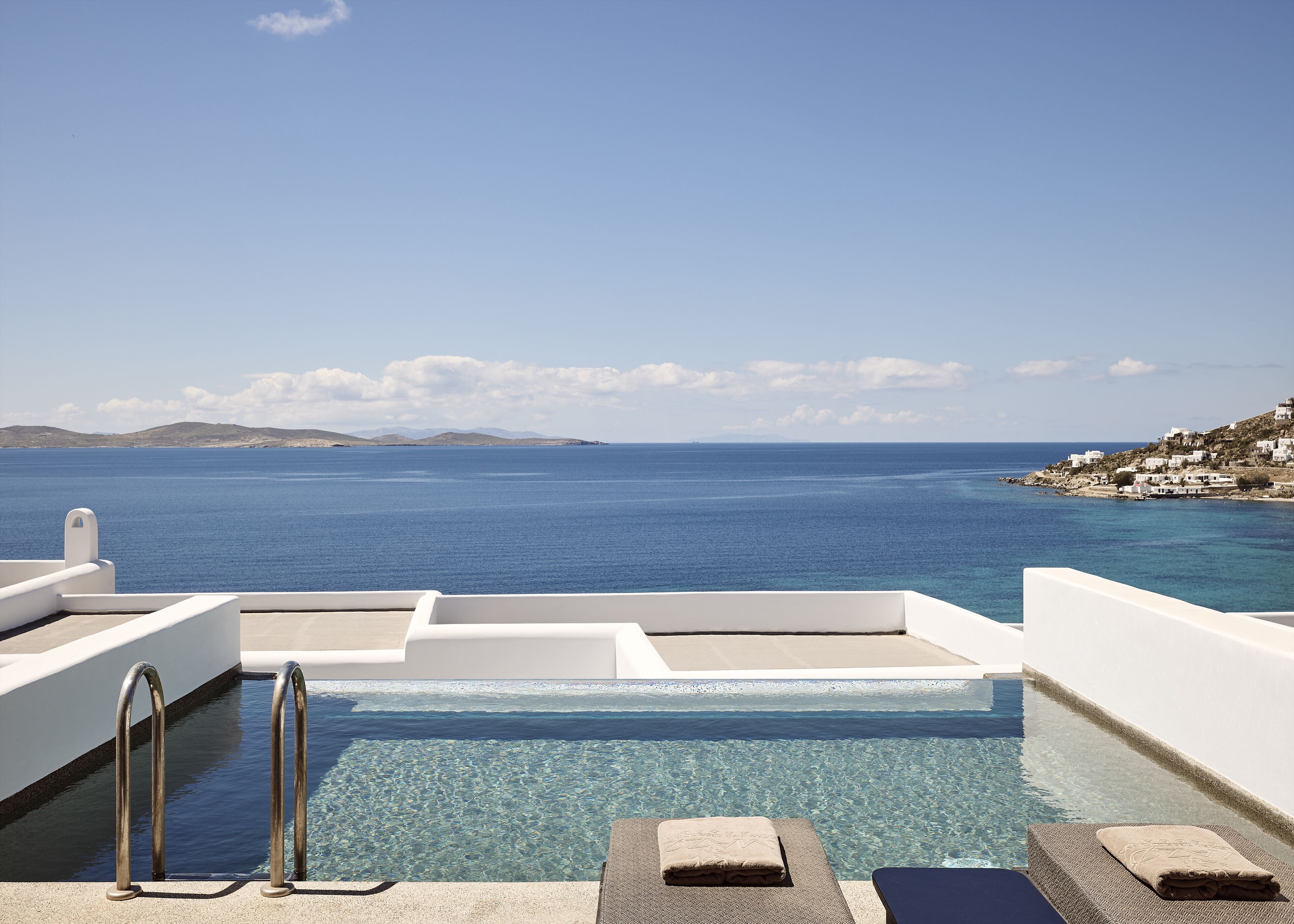 A clear blue sea view from a pool area with a white railing and a small island in the distance.