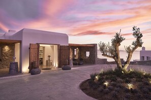 A modern building with a stone facade, wooden beams, and a stone pathway leading to the entrance. - Amazon Mykonos Resort & Spa (Mykonos)
