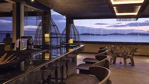 Un espace bar moderne avec vue sur l’eau, doté de meubles en bois et d’un éclairage original.