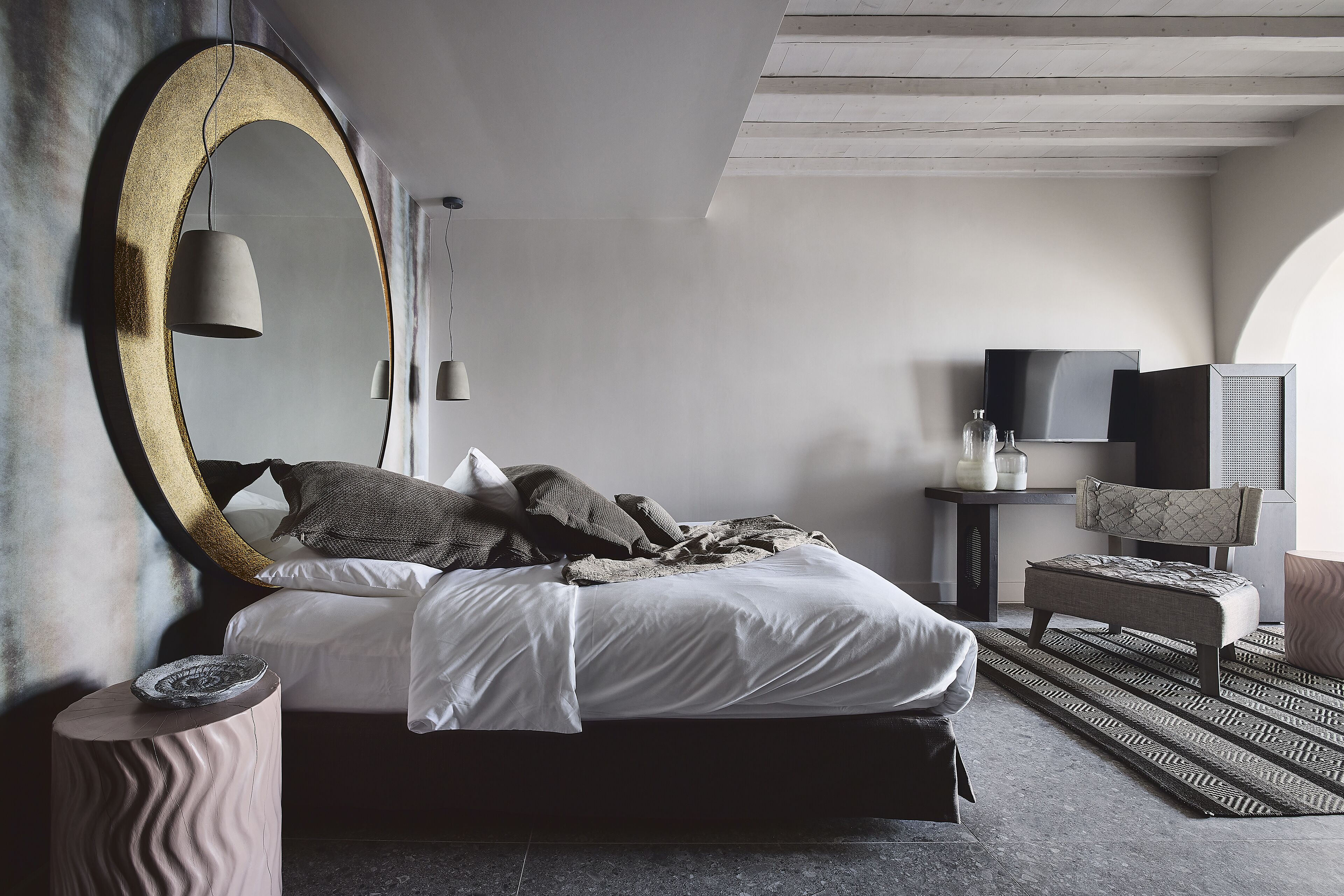 A modern bedroom with a large bed, a round mirror, a television, and a seating area.