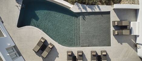 An aerial view of a swimming pool with clear water, surrounded by lounge chairs and a small garden area.