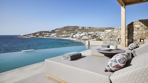 Une terrasse en bord de mer, avec un mur en pierre, une pergola en bois et une vue sur une ville côtière.