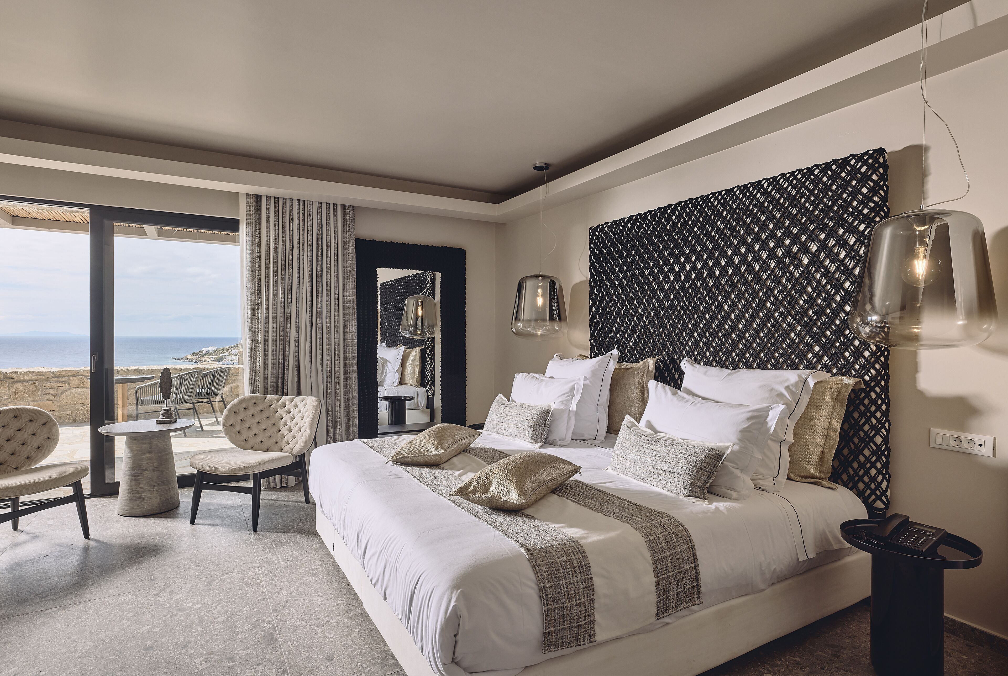 Een slaapkamer met een groot bed, uitzicht op zee, een balkon met zitplaatsen en een modern design.