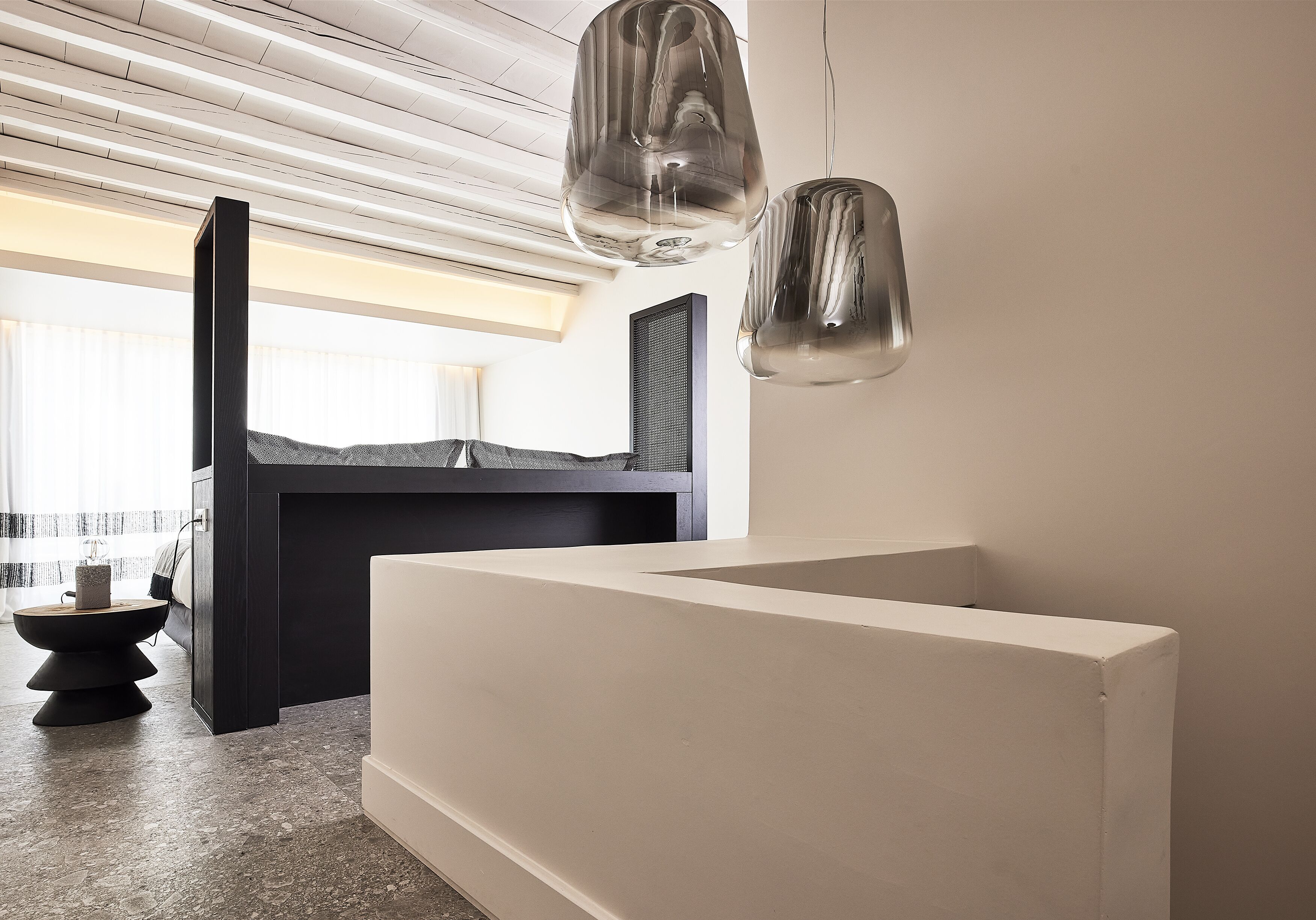 A modern interior with a minimalist design, featuring a large white console table, a dark wooden cabinet, and two hanging pendant lights.