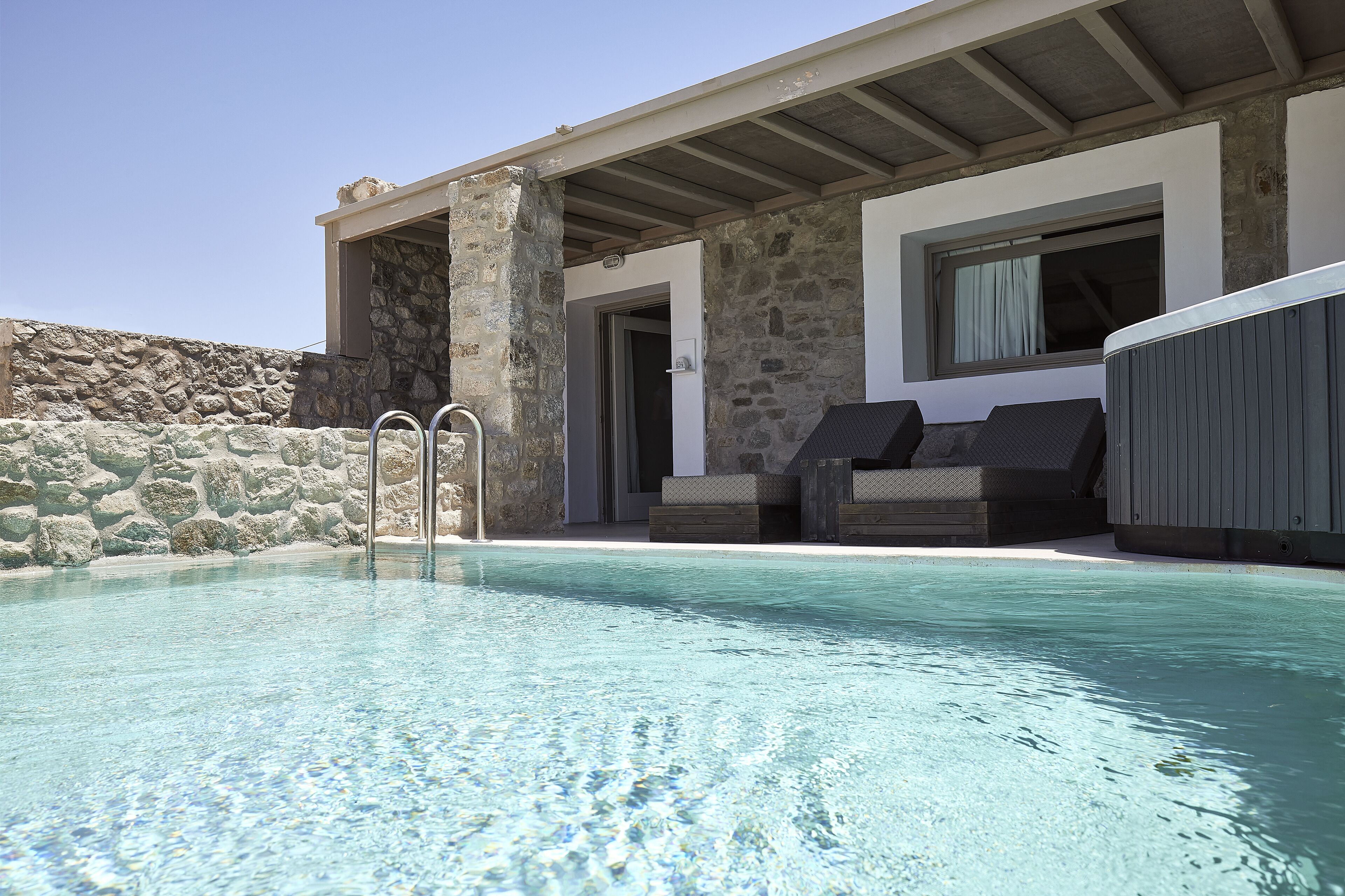 Une piscine avec des murs en pierre et un espace détente abrité.