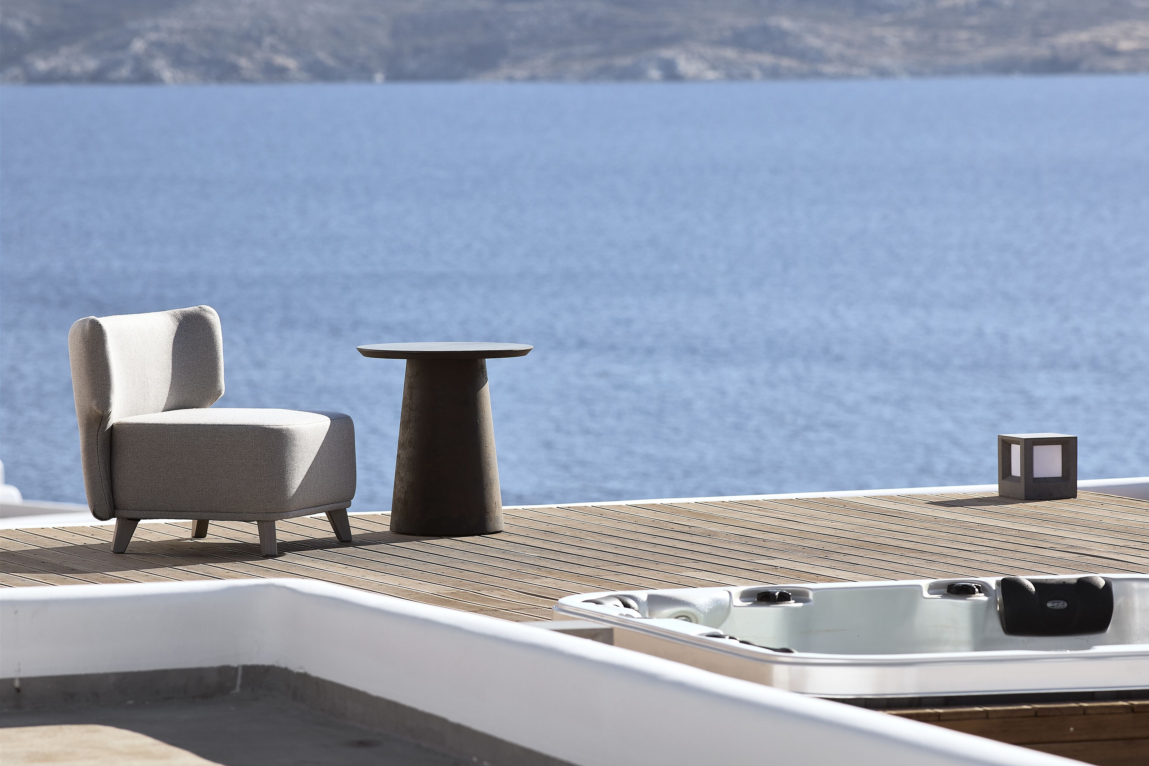 A deck with a chair, a small table, and a hot tub.