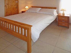 Une chambre à coucher avec un lit en bois, du linge de lit blanc, deux tables de chevet avec des lampes et une armoire en bois.