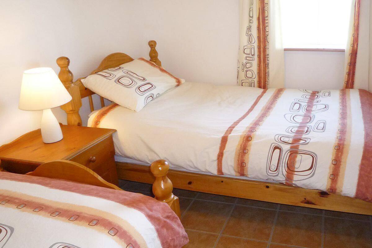 Un dormitorio con dos camas de madera, una mesita de noche con lámpara y una ventana con cortinas.