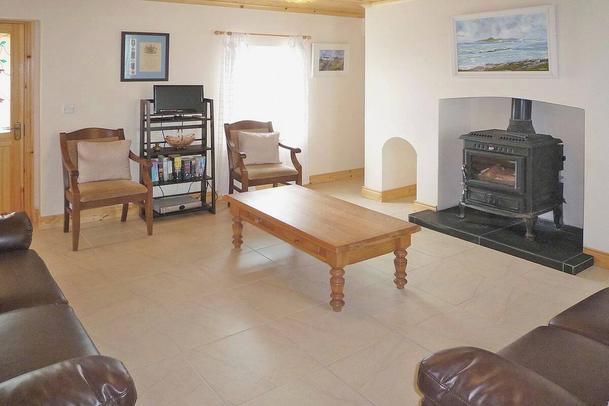 Una sala de estar con una mesa de madera, dos sillones, un mueble para televisión y una estufa de leña.