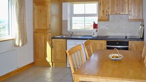 A kitchen with wooden cabinets, a dining table, chairs, a window with a view, and a fire extinguisher. - Old Barn Cottage Heir Island by Trident Holiday Homes (Heir Island)
