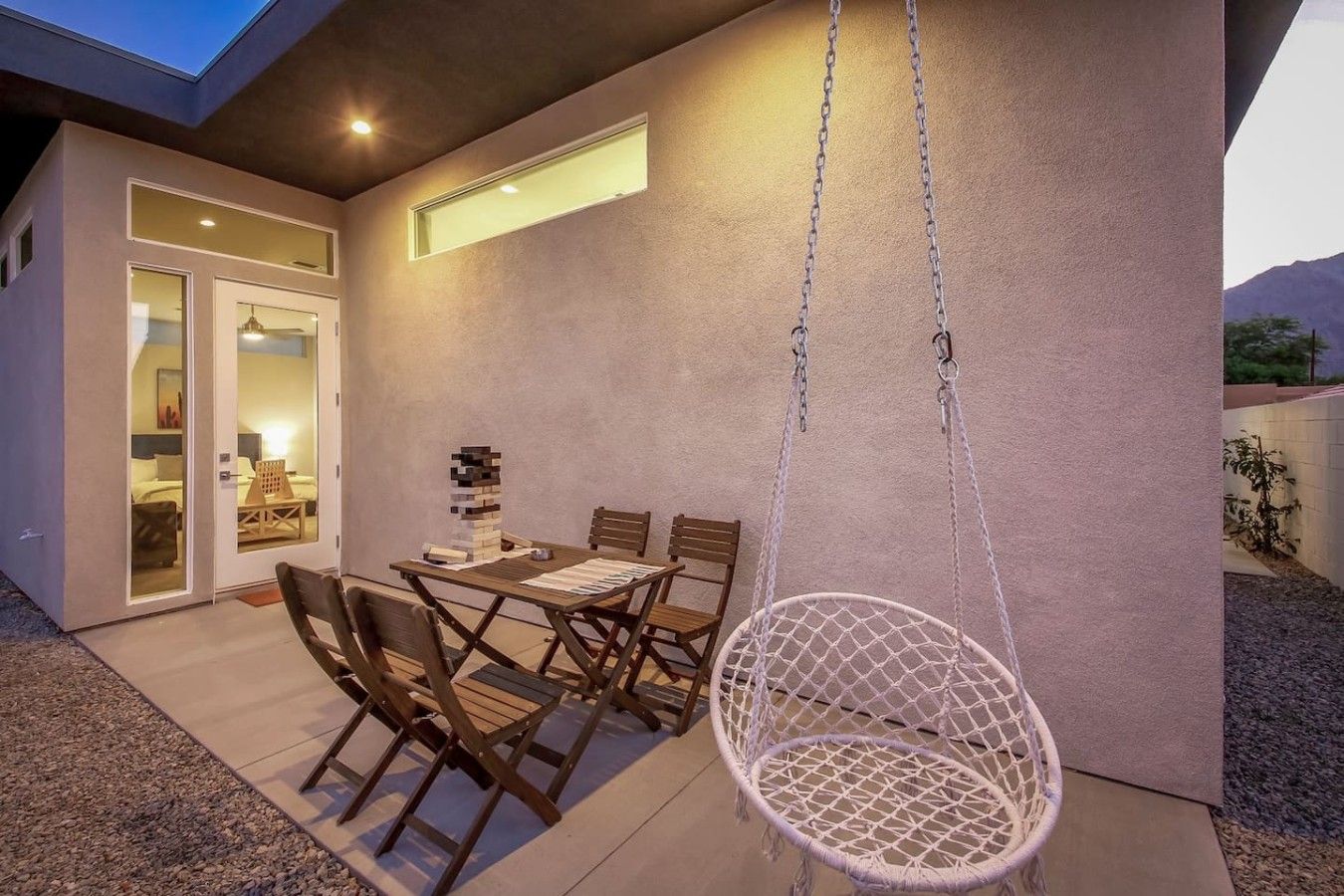 En moderne udendørs terrasse med spisebord, stole og en hængestol.