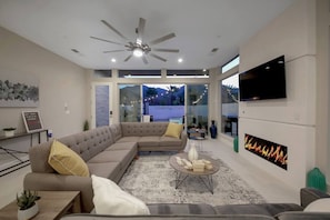 A modern living room with a sectional sofa, a flat-screen TV, a fireplace, and a ceiling fan.