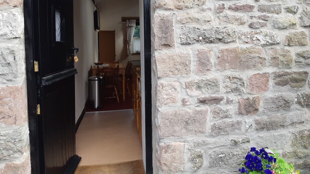Une entrée en pierre menant à un bâtiment, avec une porte noire et une petite poubelle.