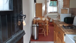 Une cuisine de taille réduite, avec des meubles de rangement en bois, un évier et une fenêtre équipée de stores.