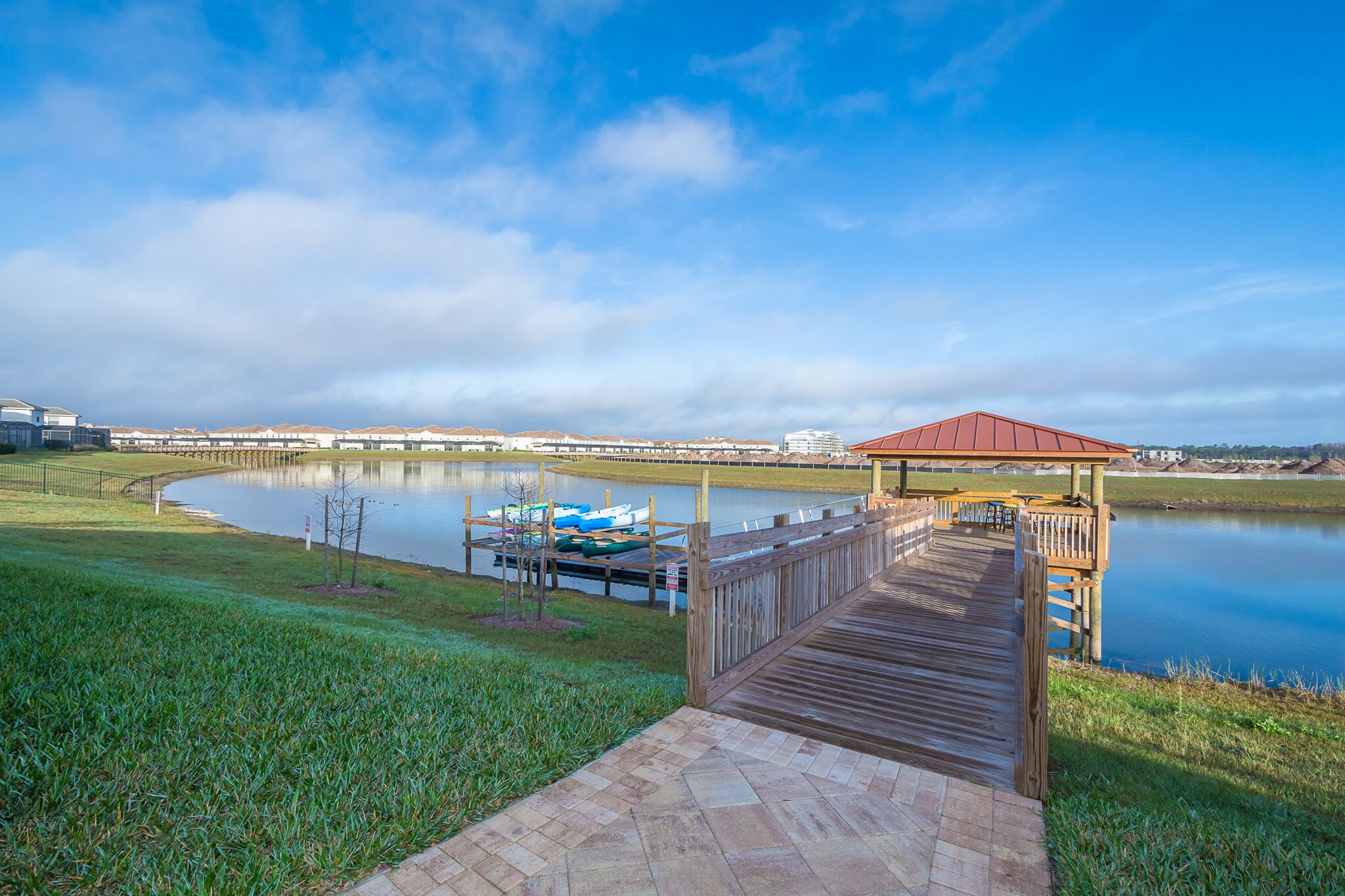 A wooden dock leading to a gazebo by a calm lake with boats docked nearby.