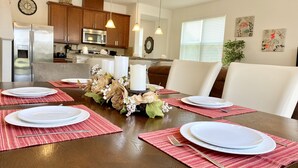 Un coin repas avec une table en bois dressée pour six personnes, entourée de chaises blanches.