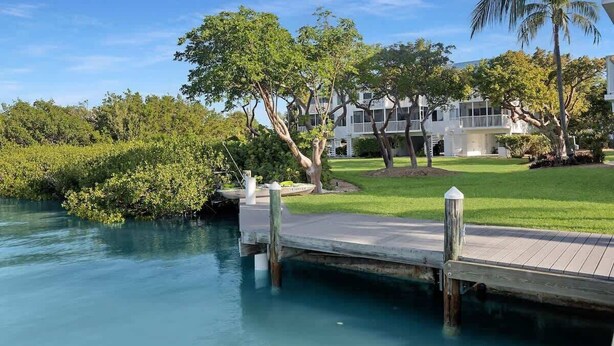 A waterfront property with a dock extending into calm water, surrounded by lush greenery and a white building with multiple balconies. - Bonefish Bungalow (MARATHON)