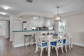 A modern kitchen with white cabinetry, a glass island counter, and a dining area with white chairs and blue cushions.
