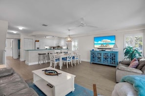 A spacious living area with a kitchen, dining area, and a large TV displaying a beach scene.