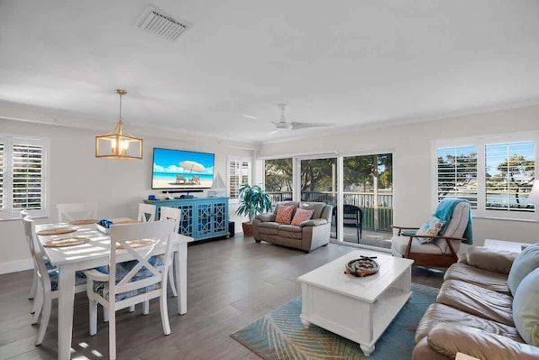 A spacious living room with a dining area, a television, and a balcony with a view.