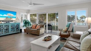 A spacious living room with a large TV, a sofa, a coffee table, and a view of the outdoors through large windows. - Bonefish Bungalow (MARATHON)