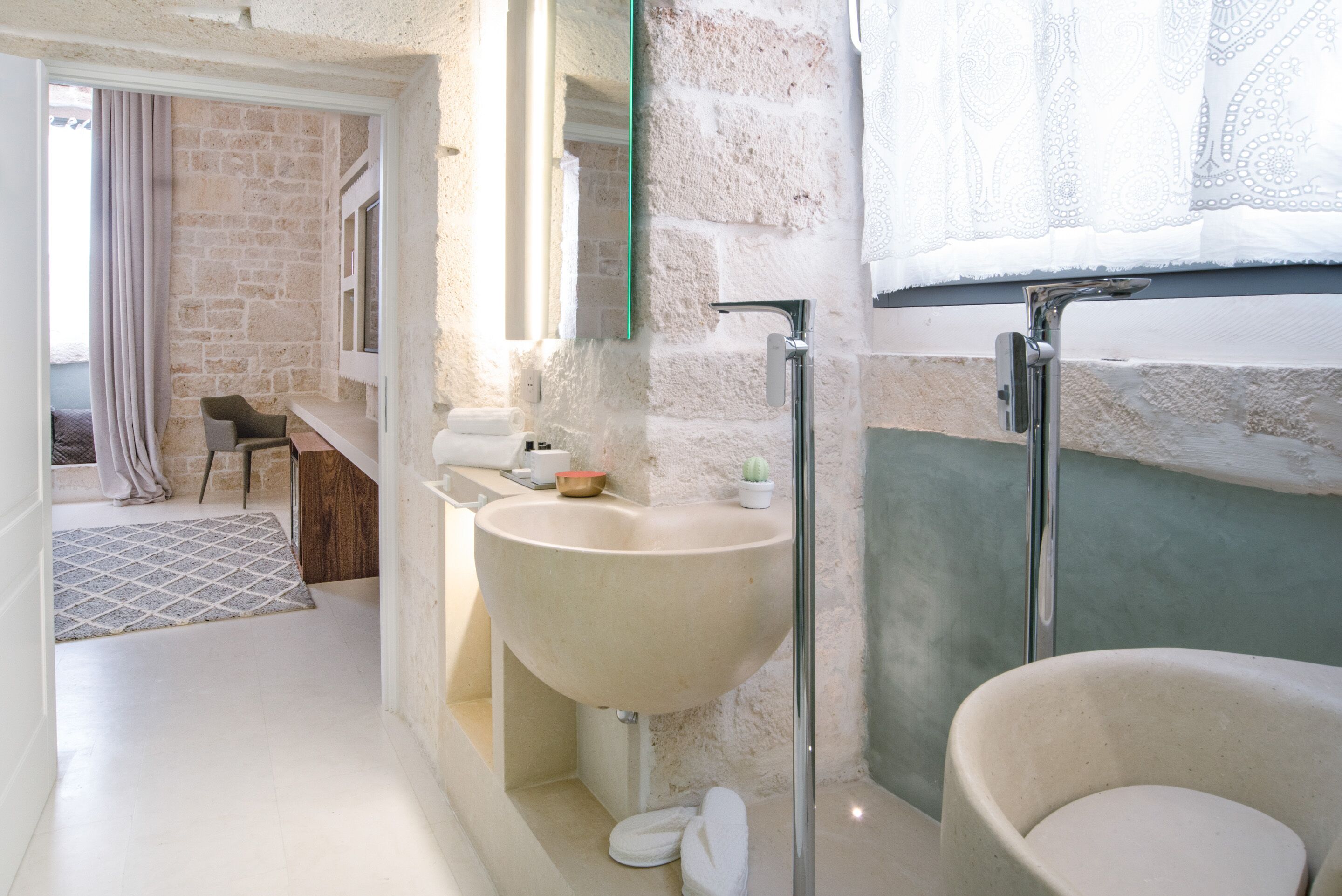 A bathroom with a large sink, a mirror, and a shower. There is a window with curtains and a view of the outside.