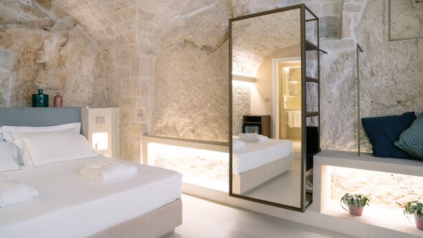 A bedroom with a stone wall, a large mirror, a bed, a bedside table, and a nightstand. - Vico Bianco (Ostuni)