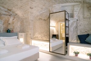 A bedroom with a stone wall, a large mirror, a bed, a bedside table, and a nightstand. - Vico Bianco (Ostuni)