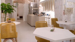 A modern kitchen with white cabinetry, a central island, and a dining area with wicker chairs and white tables. - Vico Bianco (Ostuni)