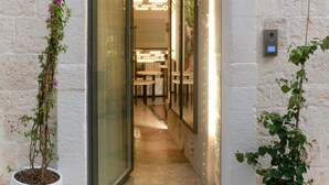 A doorway leading into a room with a stone wall, a glass door, and two potted plants on either side. - Vico Bianco (Ostuni)