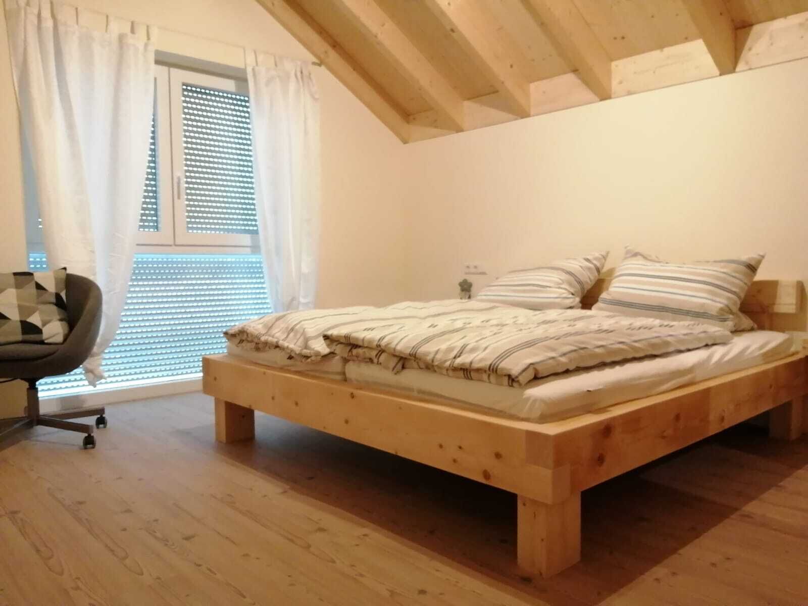 A bedroom with a wooden bed, a chair, and a window with blinds.