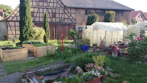 A garden with raised beds, a greenhouse, and a traditional half-timbered house.