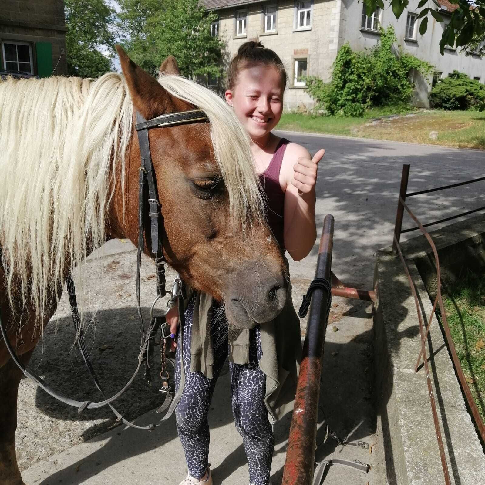 A person standing next to a horse with a harness, with a building in the background.