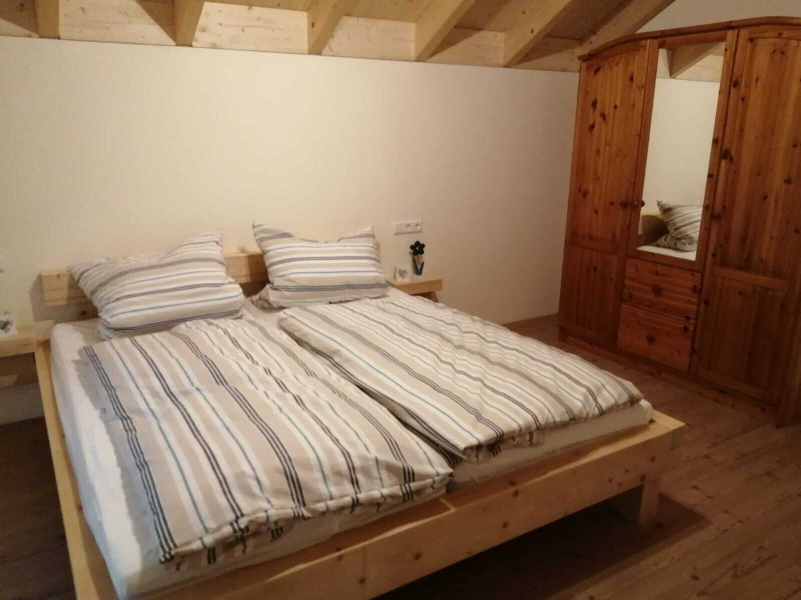 A wooden bed with striped bedding in a room with a wooden wardrobe and a small bedside table.