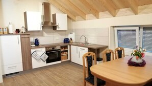 A compact kitchen with white cabinets, a wooden ceiling, and a dining area with a table and chairs.