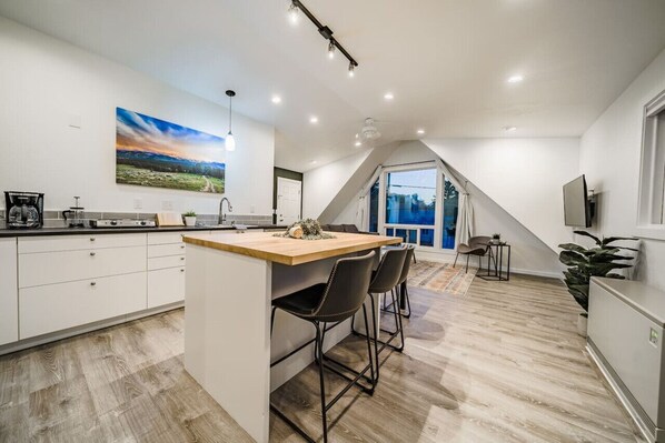 A modern kitchen with a central island, bar stools, and a large window overlooking a scenic landscape.
