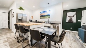 A modern kitchen with a central island, bar stools, and a dining table. - Coffee Lover`s Loft! Walk to Lake & brews. A/C (Estes Park)