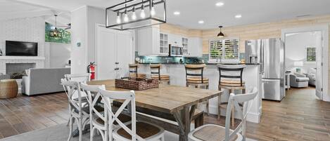 A modern kitchen with white cabinets, a wooden dining table, and a hanging light fixture.