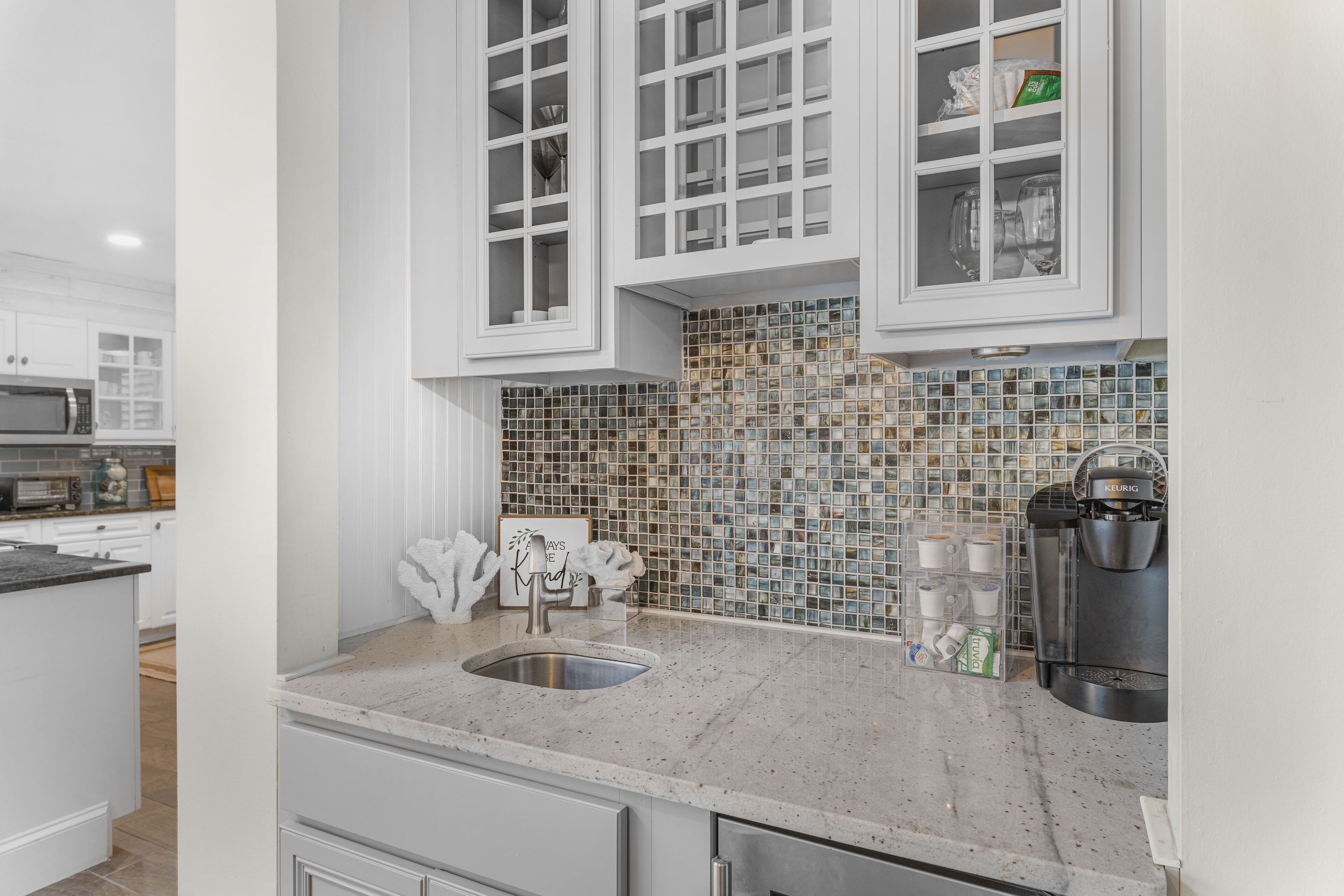 A kitchen with white cabinets, a tiled backsplash, a stainless steel sink, and a coffee maker.
