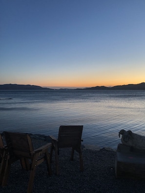 A beach with two wooden chairs facing the water, a rocky shoreline, and a sunset in the background. - Comfortable Detached House with Mountain and  Meadow views (Appin)