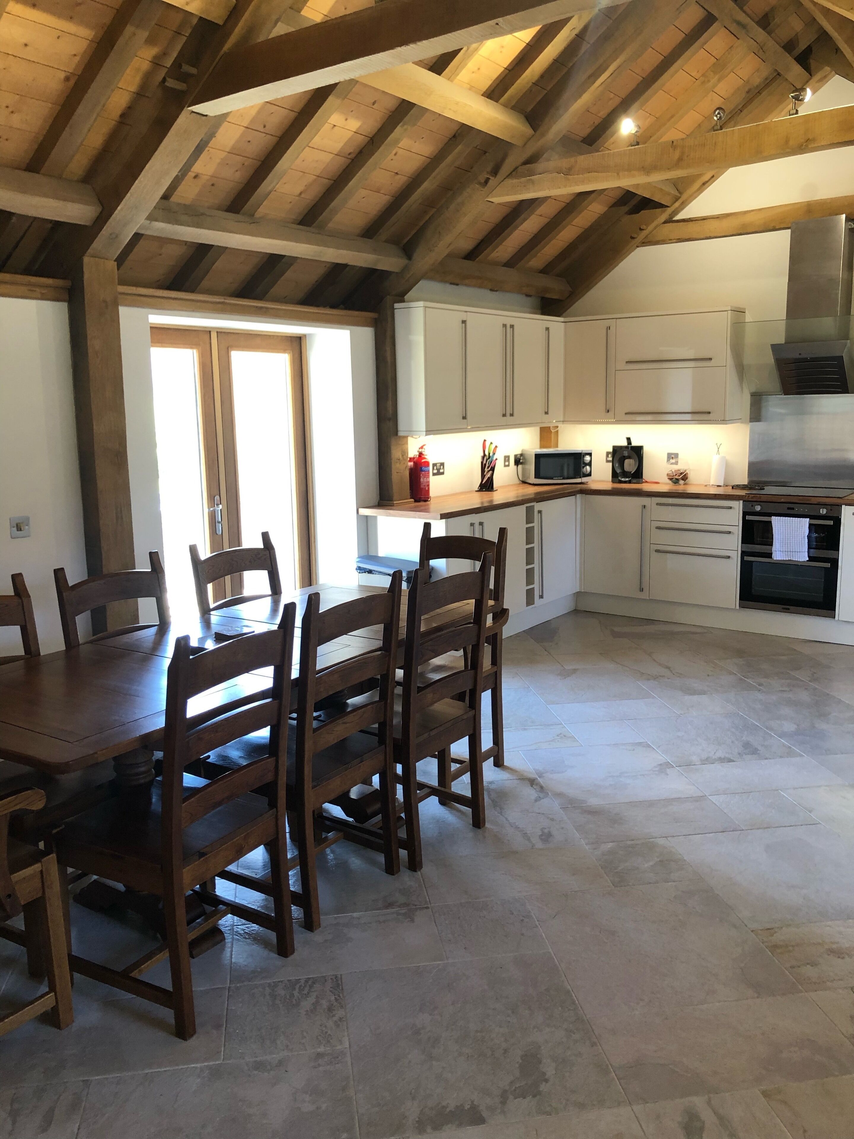 A spacious kitchen with wooden beams, a dining table with chairs, and a tiled floor.
