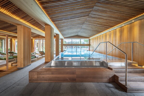 Un área de piscina interior moderna con vigas de madera y una barrera de cristal.