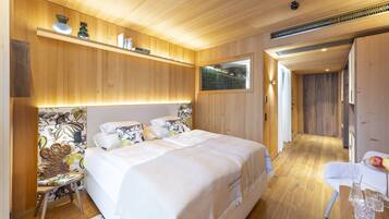 Un dormitorio moderno con techo de madera, una cama grande con ropa blanca, una mesita con un jarrón y vasos, y una silla.