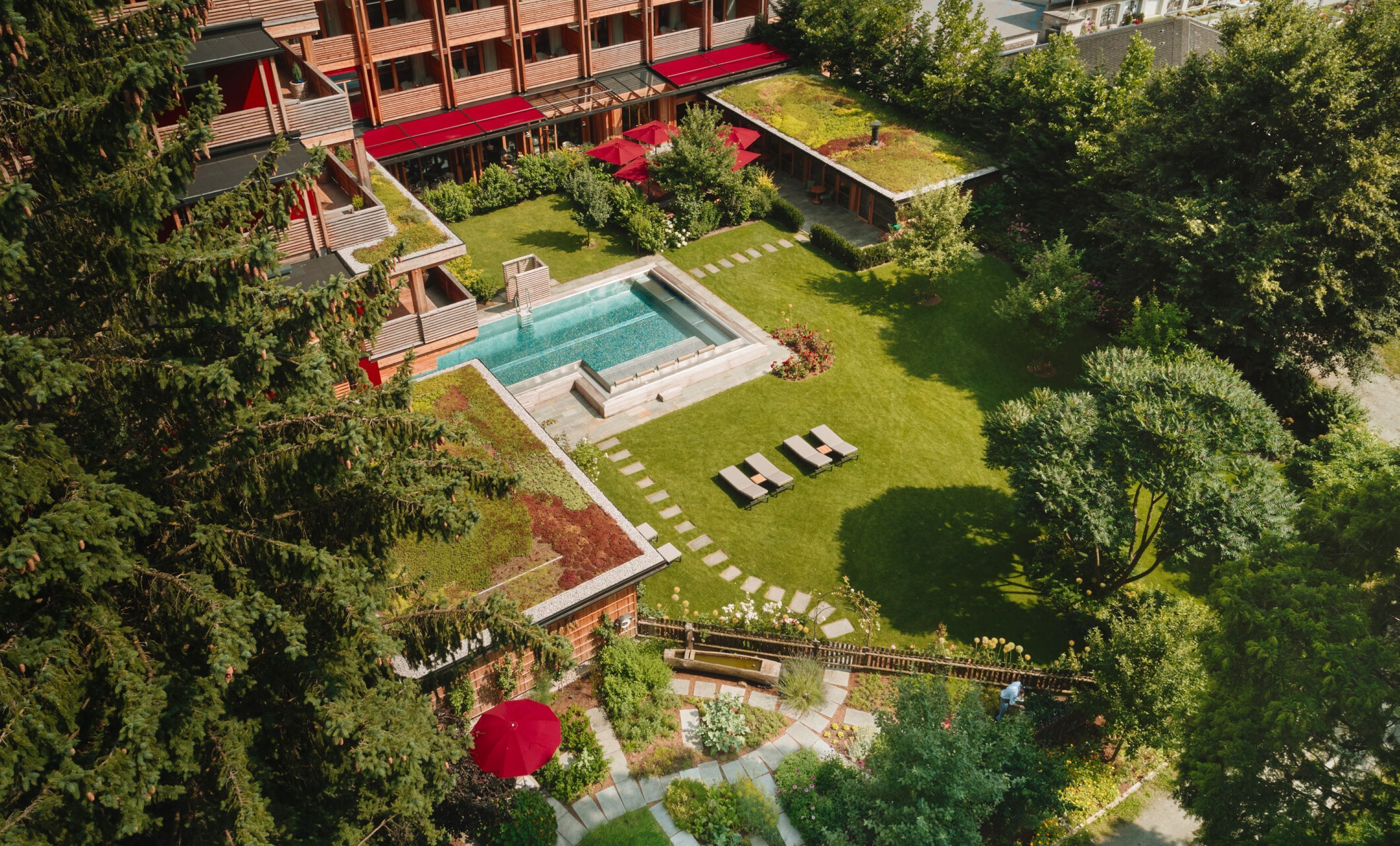 Vista aérea de un hotel con piscina, mobiliario exterior y abundante vegetación.