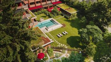Vista aérea de un hotel con piscina, mobiliario exterior y abundante vegetación.